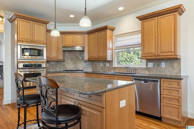 kitchen featuring under cabinet range hood, a kitchen island, a sink, appliances with stainless steel finishes, and a kitchen bar