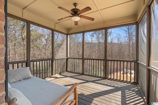 unfurnished sunroom with ceiling fan and a wooded view