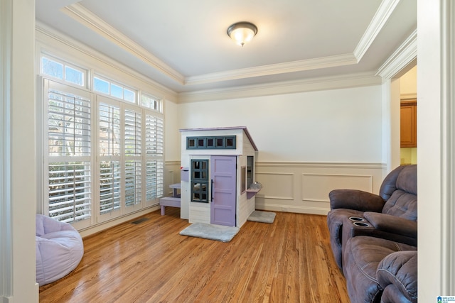 sitting room with a wainscoted wall, ornamental molding, visible vents, and light wood-style floors