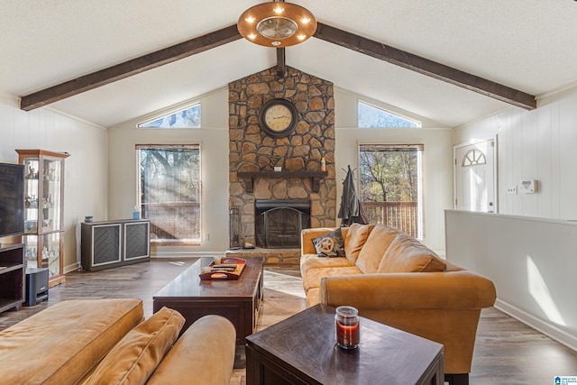 living room with vaulted ceiling with beams, a stone fireplace, wood finished floors, and a wealth of natural light