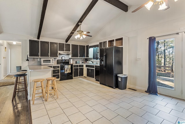 kitchen with a peninsula, under cabinet range hood, light countertops, black appliances, and a kitchen bar