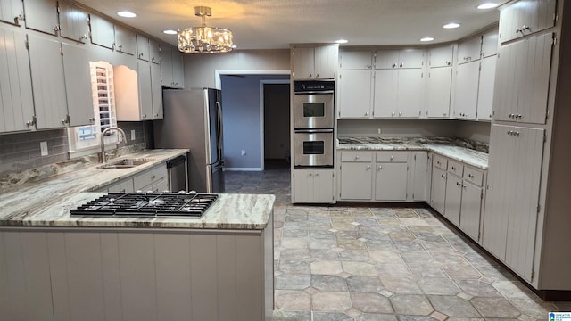 kitchen featuring stainless steel appliances, tasteful backsplash, a sink, a chandelier, and a peninsula