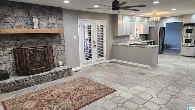 kitchen featuring a stone fireplace, a peninsula, light countertops, appliances with stainless steel finishes, and french doors