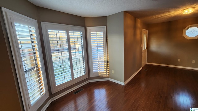 empty room featuring wood-type flooring, visible vents, a textured ceiling, and baseboards