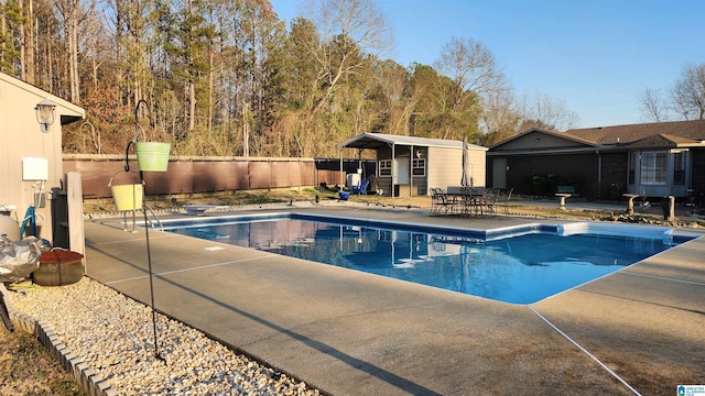 view of swimming pool with a fenced in pool, a patio area, fence, an outdoor structure, and a diving board