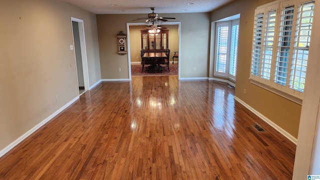 interior space featuring a textured ceiling, wood finished floors, a ceiling fan, visible vents, and baseboards