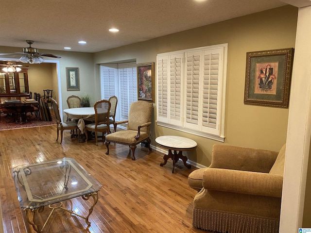 living area featuring wood-type flooring, ceiling fan, and a textured ceiling