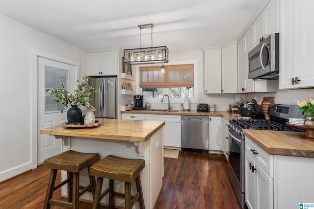 kitchen featuring dark wood-style flooring, decorative backsplash, appliances with stainless steel finishes, a sink, and butcher block countertops