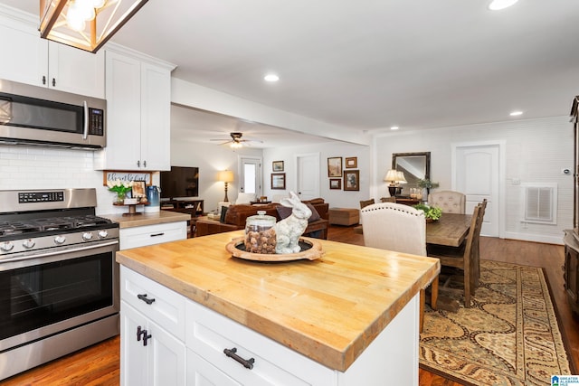 kitchen with stainless steel appliances, a ceiling fan, open floor plan, white cabinetry, and butcher block countertops