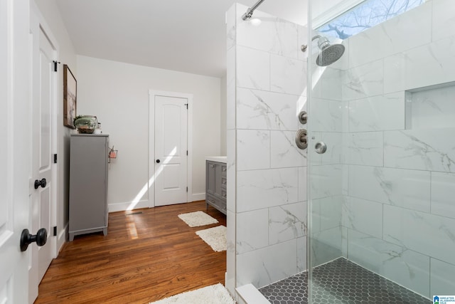 bathroom with baseboards, a tile shower, wood finished floors, and vanity