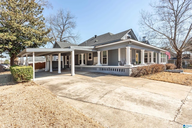 country-style home featuring a shingled roof, an attached carport, concrete driveway, and covered porch