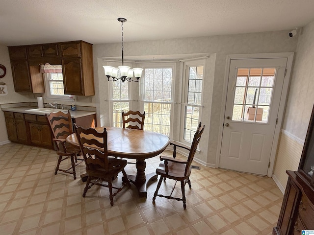 dining room featuring a chandelier, light floors, a textured ceiling, and baseboards