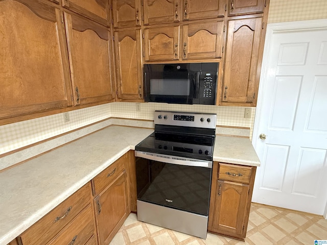 kitchen featuring light floors, electric range, black microwave, and brown cabinetry