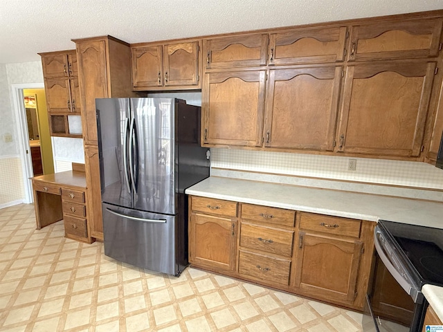 kitchen featuring brown cabinetry, freestanding refrigerator, and light floors