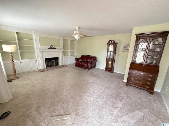 unfurnished living room with a textured ceiling, ceiling fan, carpet floors, baseboards, and a glass covered fireplace