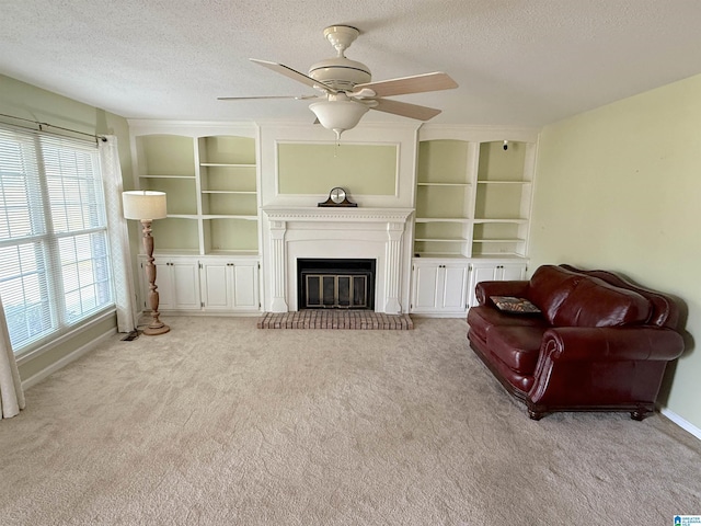 living room featuring built in shelves, a glass covered fireplace, light carpet, a textured ceiling, and baseboards