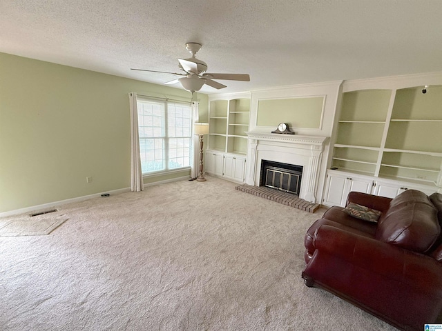 living area with a textured ceiling, a glass covered fireplace, visible vents, and light colored carpet