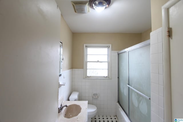 bathroom with visible vents, toilet, a wainscoted wall, a sink, and tile walls