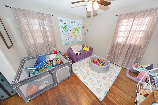 recreation room featuring a textured ceiling, wood finished floors, and a ceiling fan