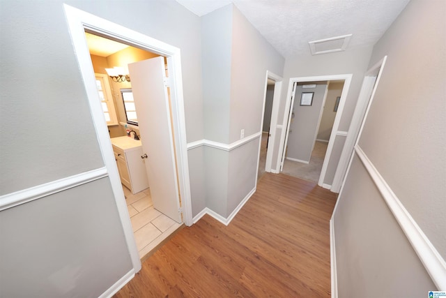 corridor featuring a sink, an upstairs landing, baseboards, light wood finished floors, and attic access