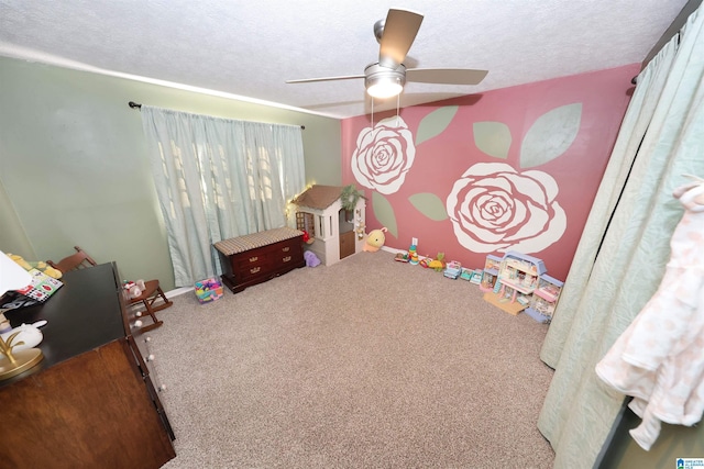 playroom featuring a textured ceiling, carpet flooring, a ceiling fan, and baseboards