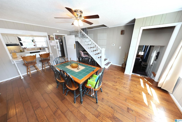 dining room featuring crown molding, ceiling fan, a textured ceiling, hardwood / wood-style floors, and stairs