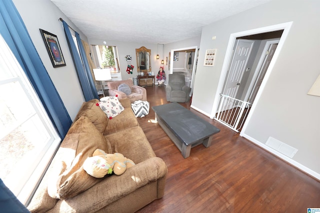 living room with a textured ceiling, wood finished floors, visible vents, and baseboards