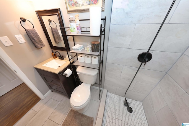 full bathroom with wood finish floors, toilet, vanity, tiled shower, and baseboards