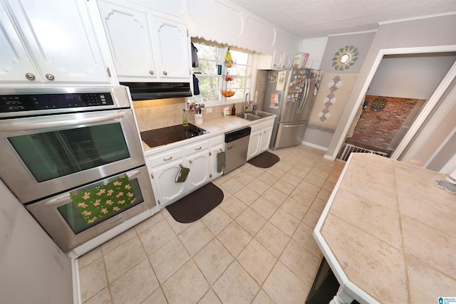 kitchen with appliances with stainless steel finishes, a textured ceiling, under cabinet range hood, white cabinetry, and a sink