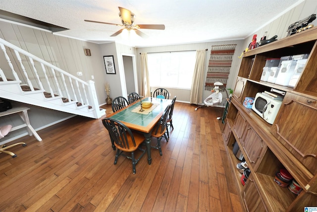 dining area with dark wood-type flooring, ceiling fan, stairway, and a textured ceiling