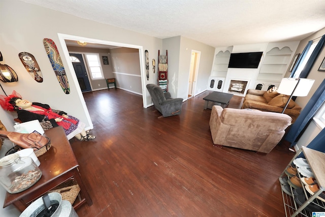 living area featuring built in shelves, a textured ceiling, baseboards, and wood finished floors