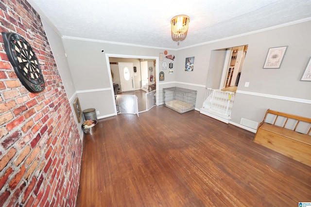 unfurnished living room with crown molding, visible vents, a textured ceiling, wood finished floors, and baseboards