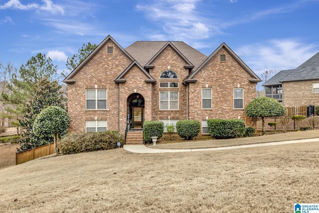 view of front of house featuring a shingled roof, fence, and brick siding