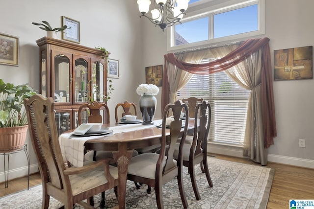 dining room with baseboards, a towering ceiling, light wood finished floors, and an inviting chandelier