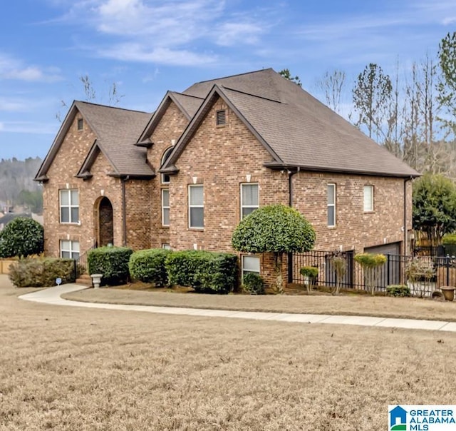 view of front of home with brick siding, roof with shingles, a front yard, and fence