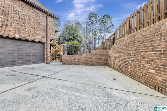 view of side of property with brick siding, fence, a garage, driveway, and stairs