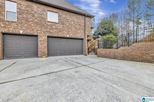 view of property exterior with a garage, concrete driveway, brick siding, and stairway