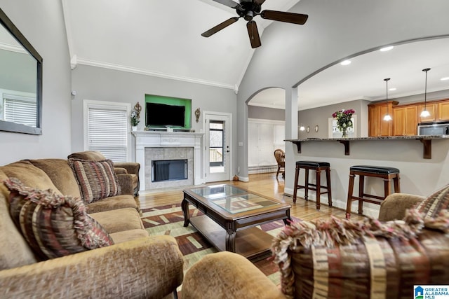 living area featuring ceiling fan, a fireplace, baseboards, ornamental molding, and light wood-type flooring