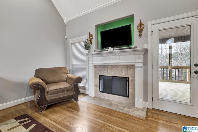 living area featuring baseboards, crown molding, a tiled fireplace, and wood finished floors