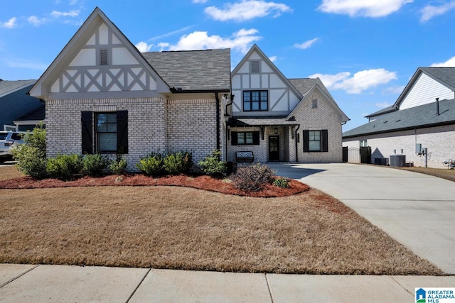 tudor home featuring brick siding, central AC unit, concrete driveway, and a front yard