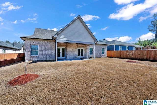 rear view of house with a yard, french doors, brick siding, and a fenced backyard