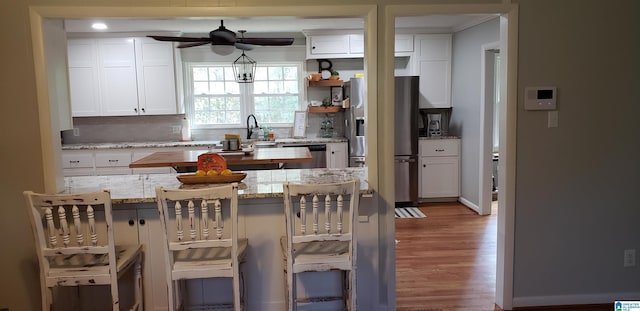 kitchen with light stone counters, a breakfast bar, white cabinetry, ceiling fan, and stainless steel fridge with ice dispenser