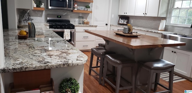 kitchen with stainless steel appliances, butcher block countertops, white cabinets, a kitchen breakfast bar, and open shelves