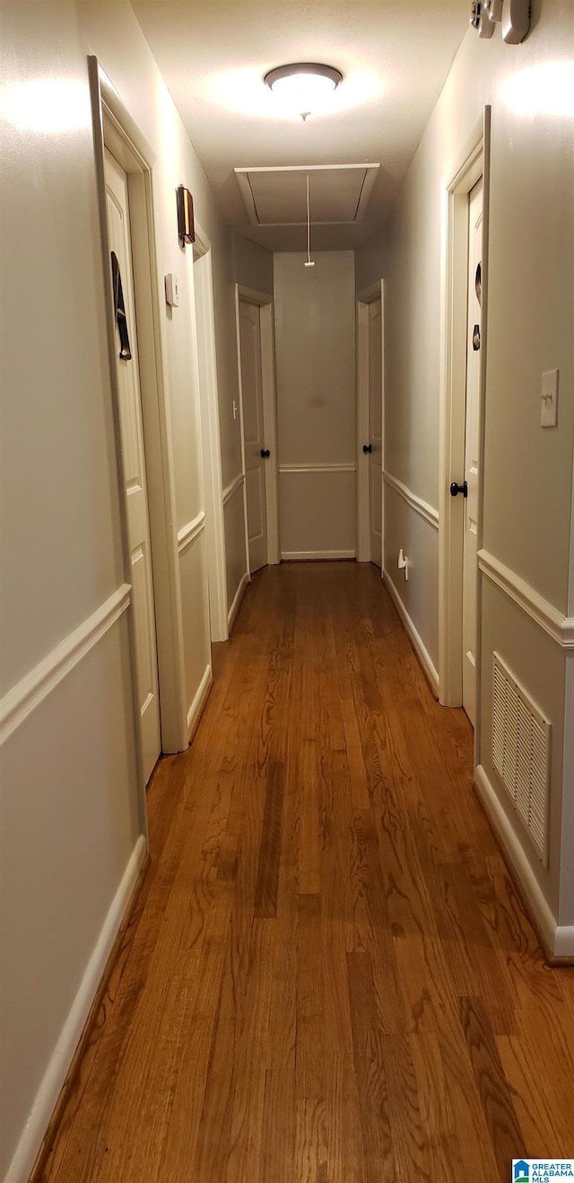 hall featuring attic access, visible vents, baseboards, and wood finished floors