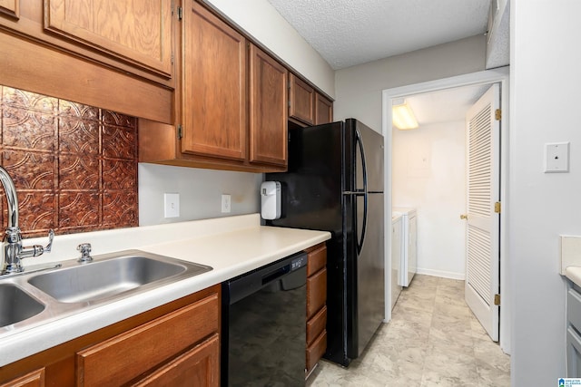 kitchen with washer and clothes dryer, a sink, light countertops, black appliances, and brown cabinetry