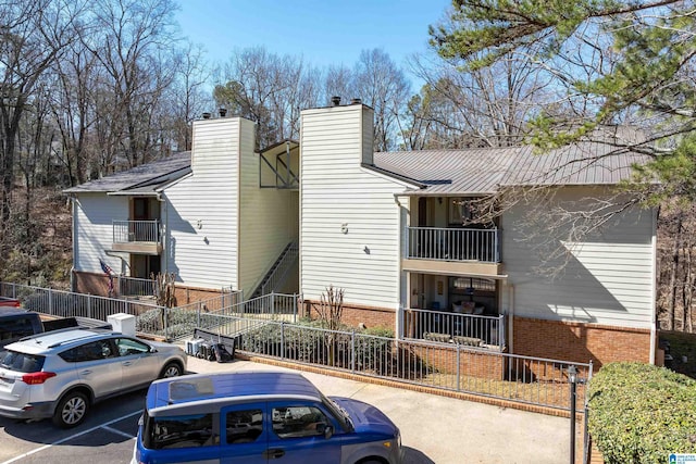 exterior space featuring a chimney, fence, uncovered parking, and brick siding