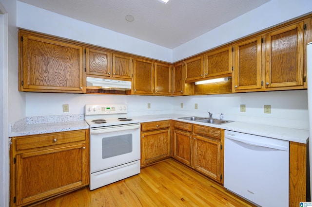 kitchen featuring white appliances, light wood finished floors, light countertops, under cabinet range hood, and a sink