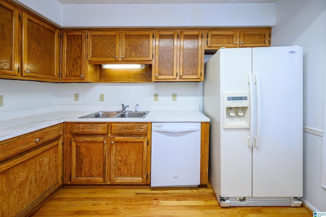 kitchen with brown cabinetry, white appliances, a sink, and light wood finished floors