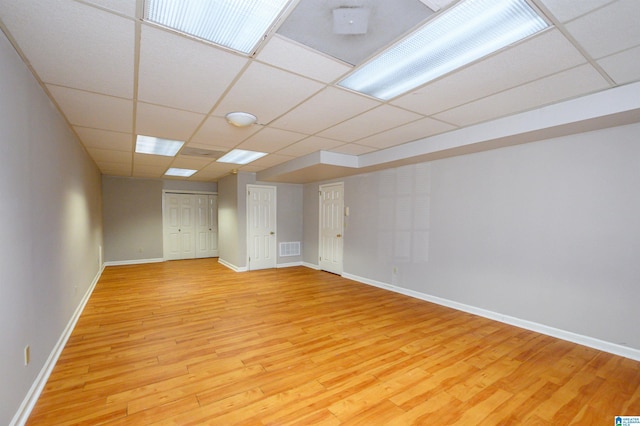 empty room with visible vents, light wood-type flooring, a paneled ceiling, and baseboards