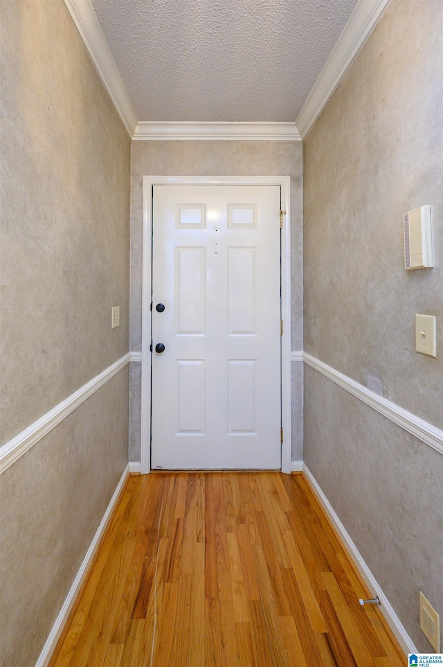 doorway featuring light wood-style flooring, visible vents, ornamental molding, and a textured ceiling